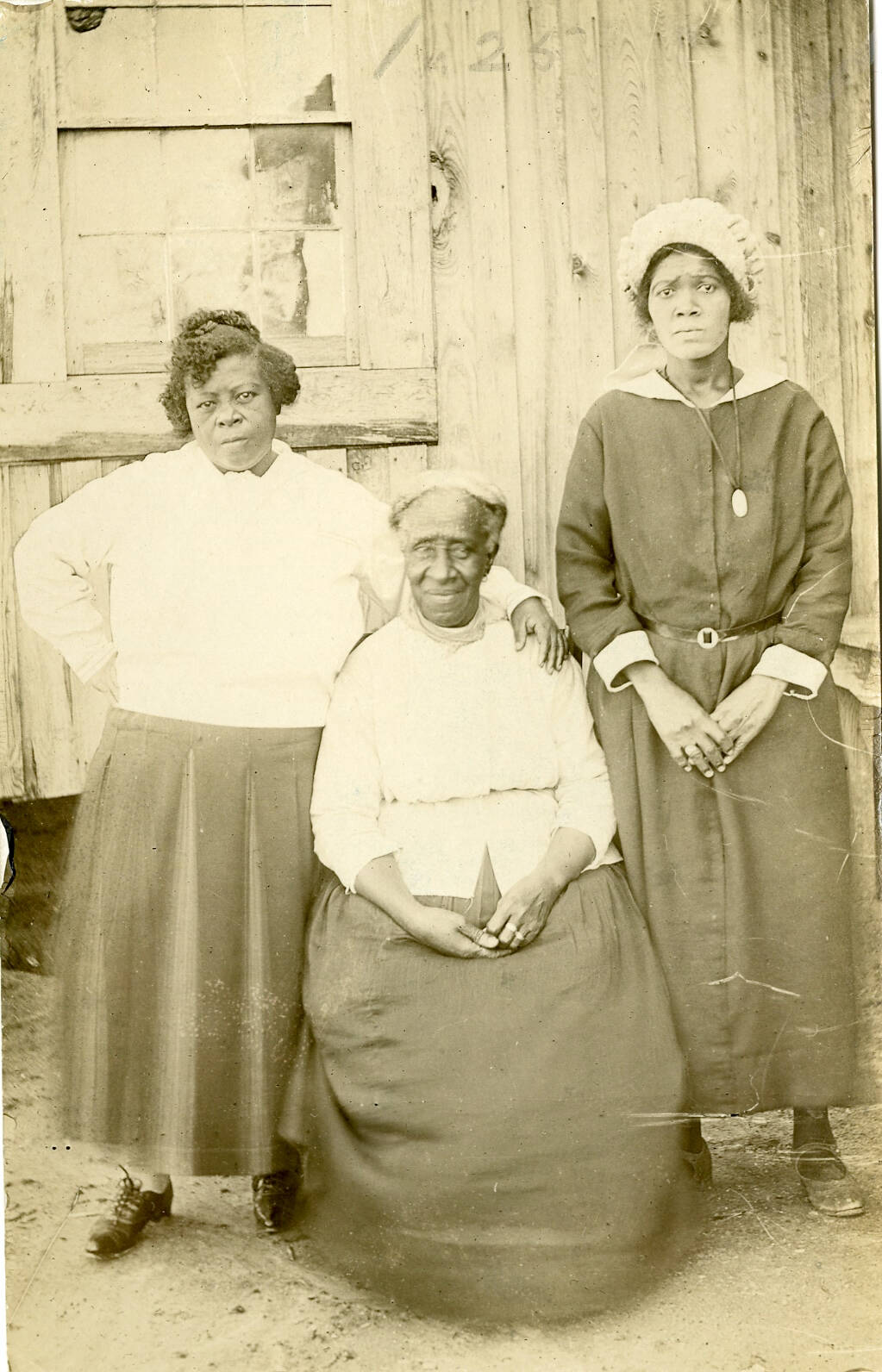Black and white real photo postcard of three women outside of a house or barn.